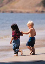 Little girl and boy running on the beach holiding hands
